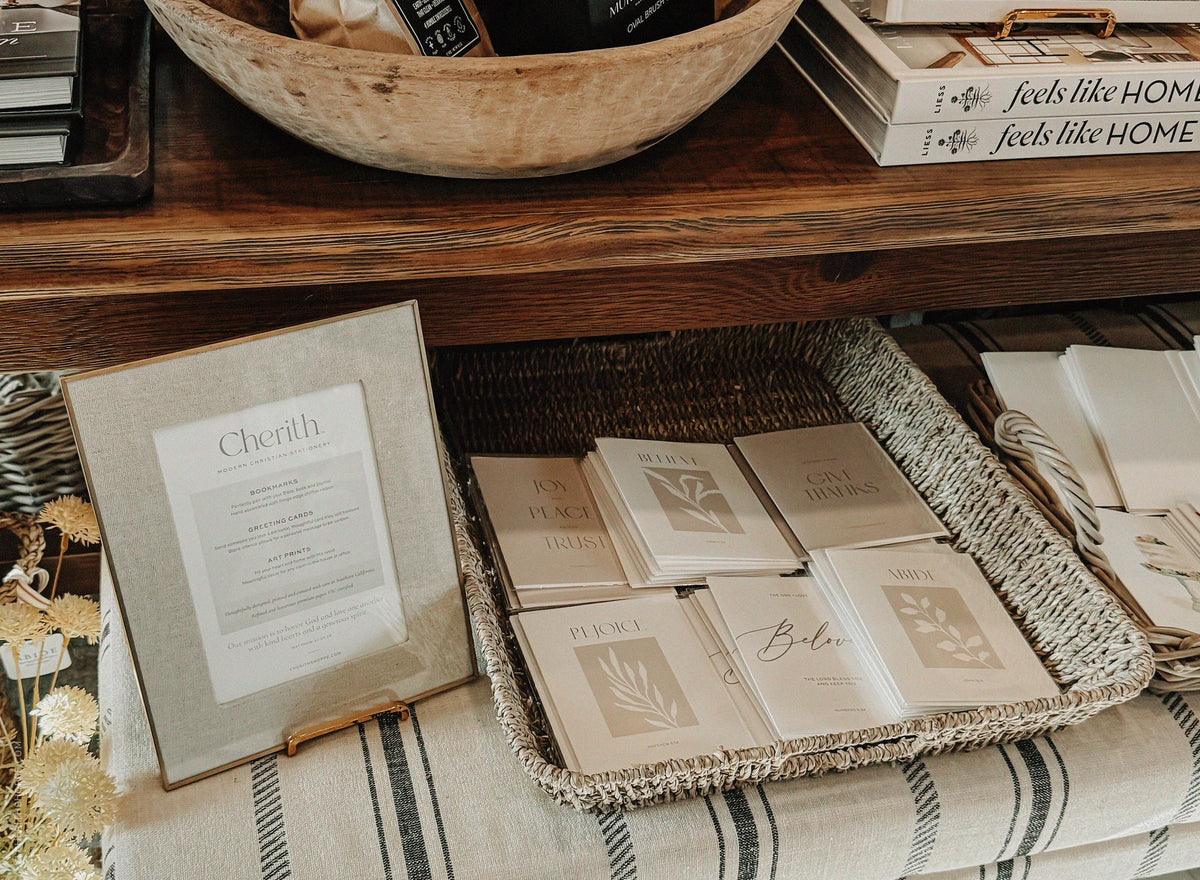 Cherith greeting cards and framed brand sign displayed in a woven basket at a boutique retailer.