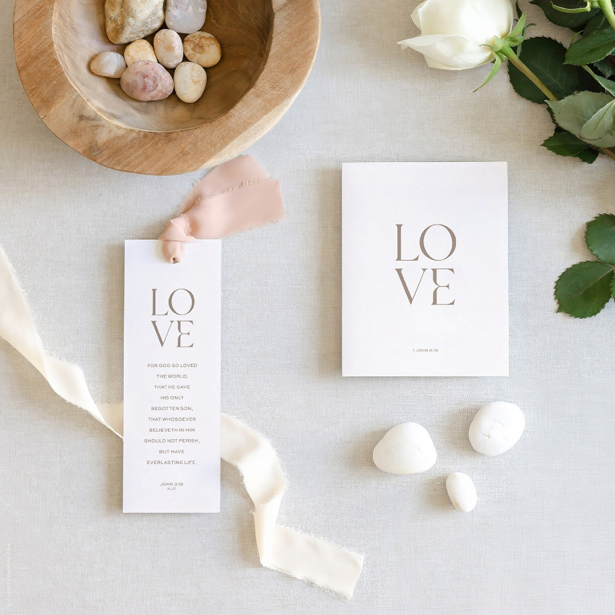 LOVE John 3:16 bookmark with blush ribbon and LOVE 1 John 4:19 card on linen with white roses.