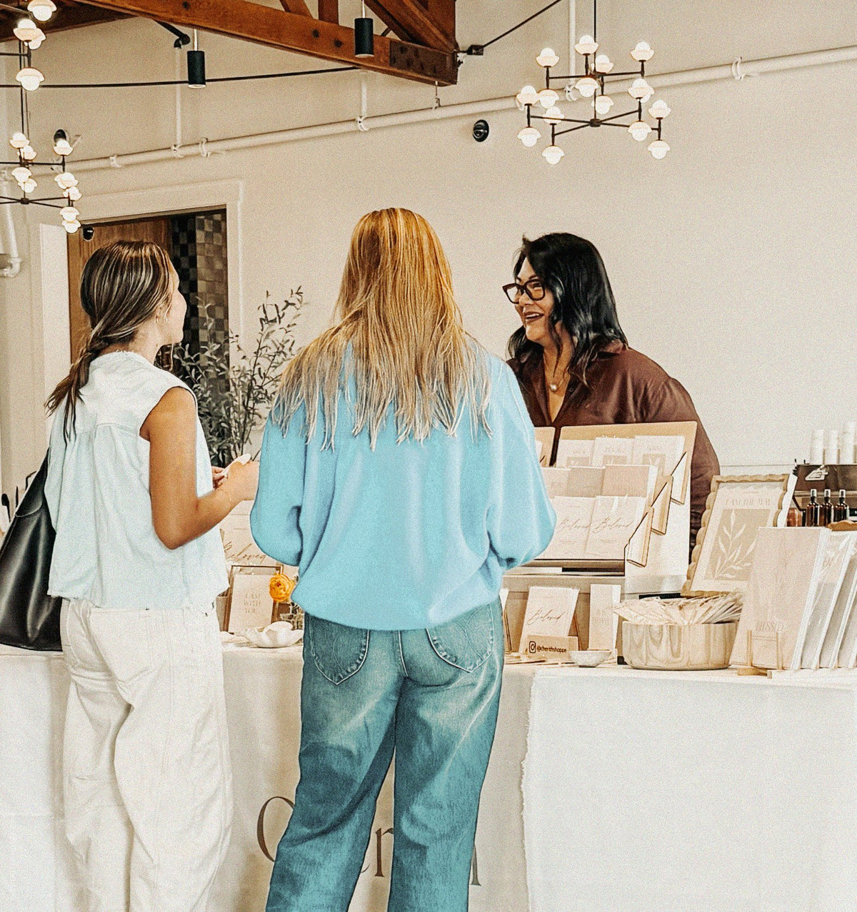 Shoppers browsing Cherith cards and art prints at a market booth.